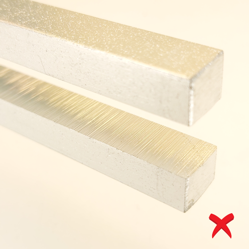 Two silver rectangular metal bars with fine brushed grooves, angled diagonally, plus a red X suggesting not allowed or incorrect.